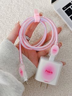 a person holding a pink and white cord next to a laptop