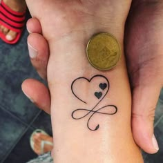 two people holding hands with tattoos on their wrists and one has a coin in the other hand