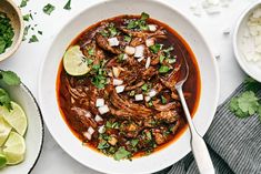 a white bowl filled with meat and vegetables next to bowls of rice, limes and cilantro