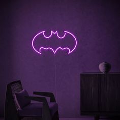 a purple neon batman sign in a dark room with a black chair and table next to it