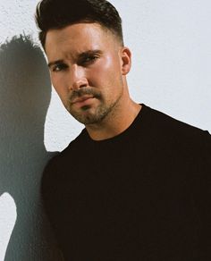 a man standing in front of a white wall with his shadow on the wall behind him