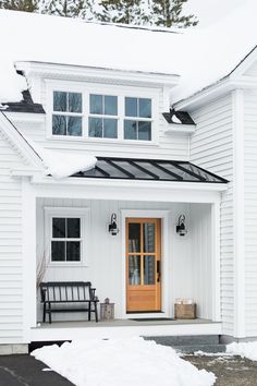 a white house with snow on the ground and a wooden door in front of it