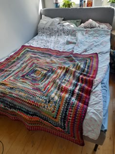 a crocheted blanket is laying on the bed with pillows and blankets around it