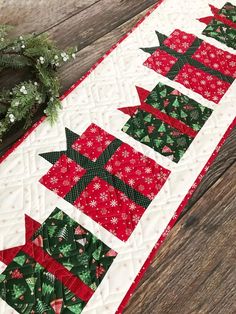 a quilted table runner with red and green christmas trees on it next to a wreath