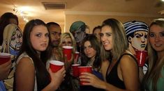 a group of young women holding red cups in front of a wall with cartoon faces on it