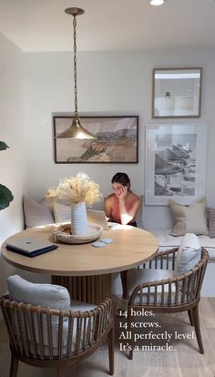 a woman sitting at a round table in a living room with white walls and wood flooring