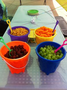 four buckets filled with grapes and other fruits on a table outside at a party