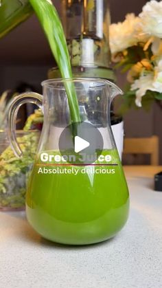 a green liquid is being poured into a glass pitcher with white flowers in the background