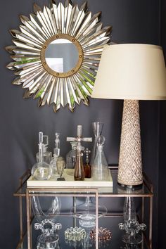 a table topped with lots of glass bottles and a lamp next to a wall mounted mirror