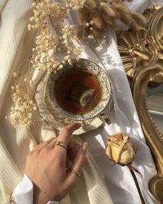 a person is holding a spoon near a tea cup on a table with dried flowers