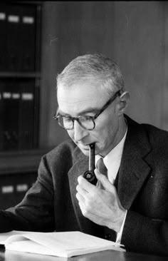 an old man sitting at a desk with a pen in his hand and looking through a book