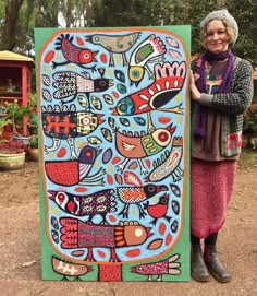 a woman standing next to a large painting on the side of a road with trees in the background