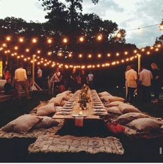 an outdoor dining area with lots of lights strung over the table and pillows on the ground