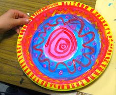 a child's hand is holding a paper plate with an art project on it