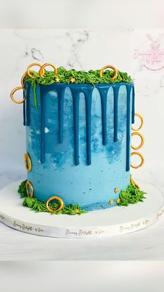 a blue cake decorated with gold rings and greenery