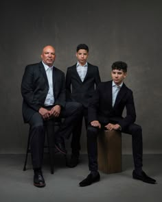 three men in suits are sitting on a stool