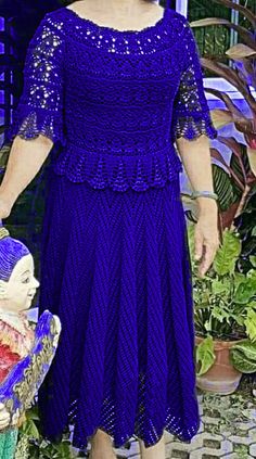 a woman in a purple dress standing next to a small doll and potted plant