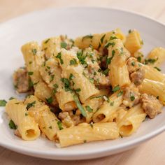 a white plate topped with pasta covered in meat and parsley on top of a wooden table