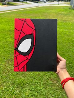 someone is holding up a card with a spiderman face on it in the grass