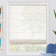 a window with white roman shades and pictures on the wall above it, along with a blue chair