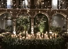 an indoor venue with candles and flowers in the center, surrounded by greenery at night