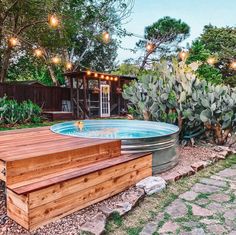 a hot tub in the middle of a garden with lights hanging from it's roof