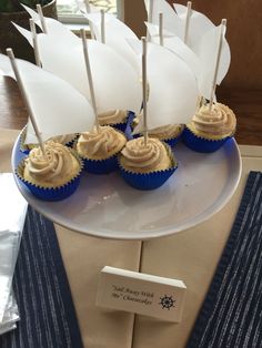 cupcakes with sailboats on them are sitting on a white plate and blue napkins