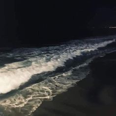 there is a wave coming in to the shore line at night with lights shining on it