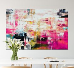 an abstract painting on the wall above a table with chairs and vase filled with flowers