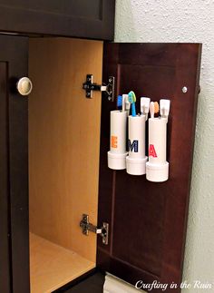 an open cabinet with three toothbrushes and one tube on it's door