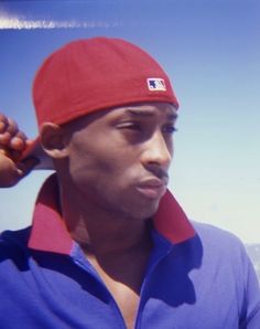 a young man wearing a red and blue baseball cap with his hand on his ear