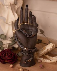 a hand with rings and bracelets on it sitting next to some fake flowers in front of a statue