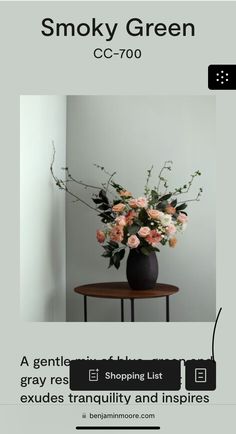 a black vase filled with pink flowers sitting on top of a table next to a white wall