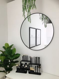 a mirror hanging on the wall above a table with makeup brushes and brush holders in front of it