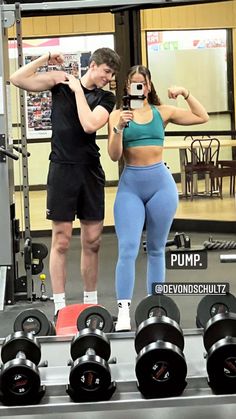 a man and woman standing in front of a gym machine with dumbs on each side