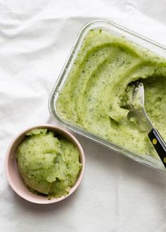 a bowl of guacamole next to a spoon on a white tablecloth