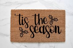 a door mat that says tis the season with black lettering on it and holly decorations