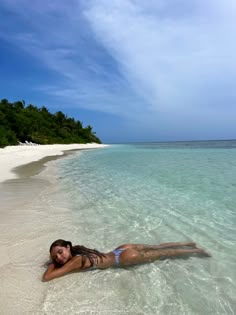 a woman laying on top of a sandy beach next to the ocean with clear blue water