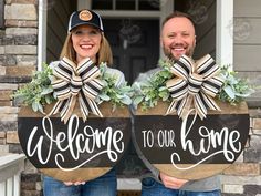 two people holding welcome to our home signs with greenery on the front and back