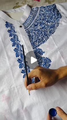 someone is using a pen to draw on a white shirt with blue and white designs