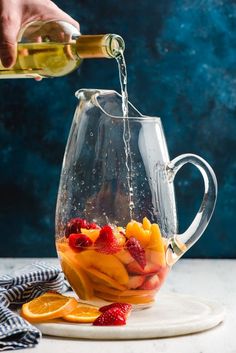 someone pouring liquid into a pitcher filled with fruit