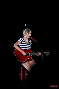 a woman sitting on top of a stool while holding a guitar in front of a microphone