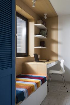 a room with a bed, desk and chair next to a blue door in it