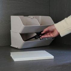 a person using scissors to cut paper in a holder on a desk next to a laptop