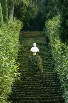 a white statue sitting on top of a set of steps in the middle of trees