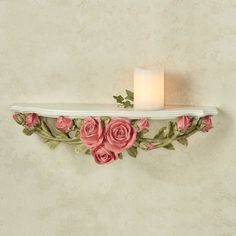 a candle that is on top of a shelf with pink flowers and leaves around it