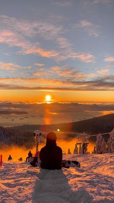 a person sitting on top of a snow covered ski slope at sunset with the sun in the distance