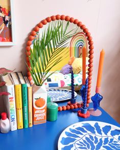 a blue table topped with books next to a mirror and candle holder on top of it