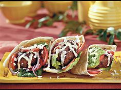 two pita sandwiches with meat, lettuce and tomato on a yellow tray