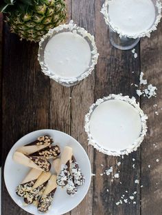 pineapple and coconut milkshakes are served in small bowls on a wooden table